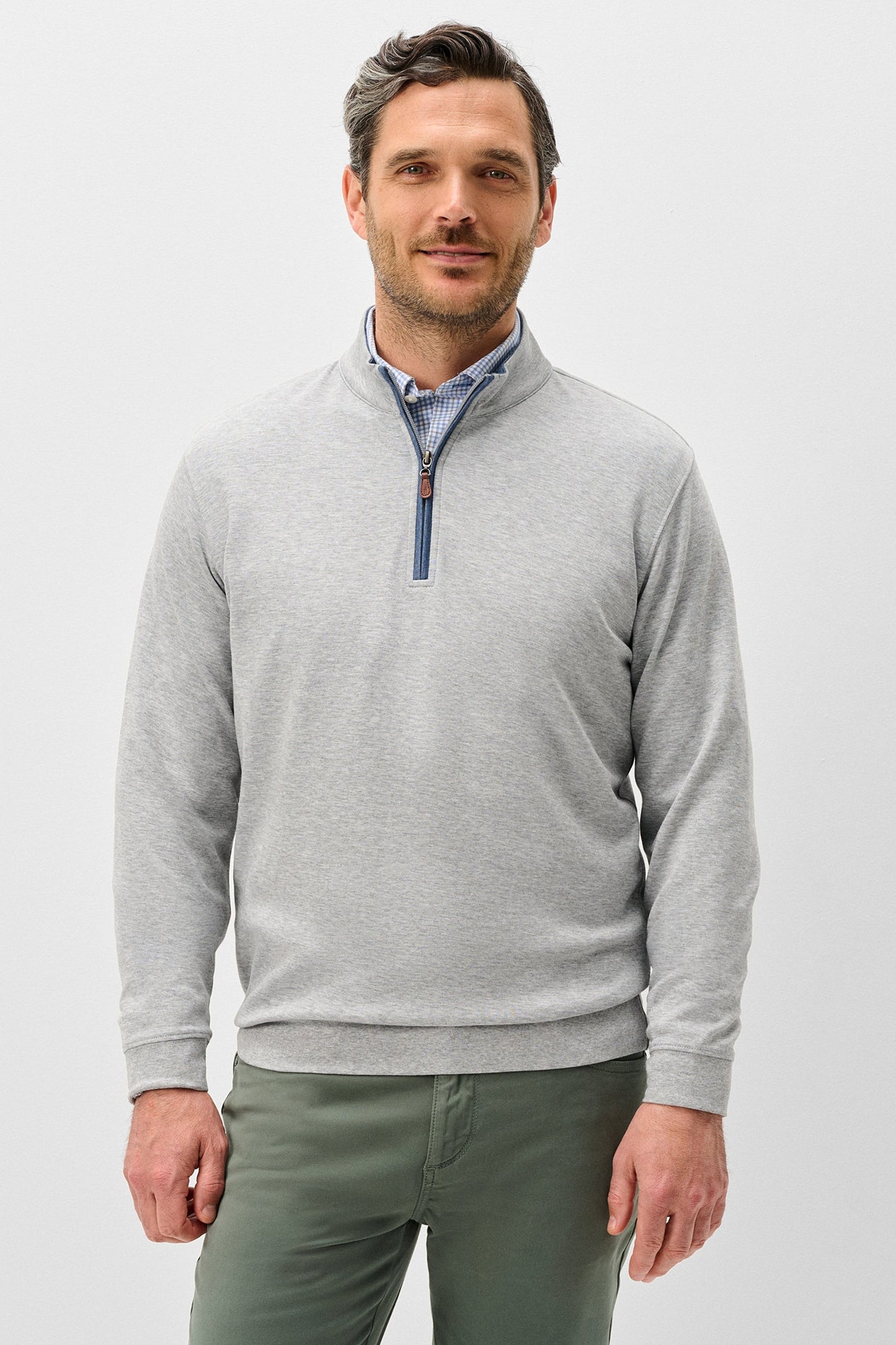 Man wearing a gray quarter-zip sweater and green pants on a light gray background