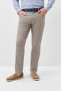 A man wearing slim-fit taupe trousers, a blue checkered shirt, a dark blue belt, and brown suede loafers, standing against a light gray studio background.
