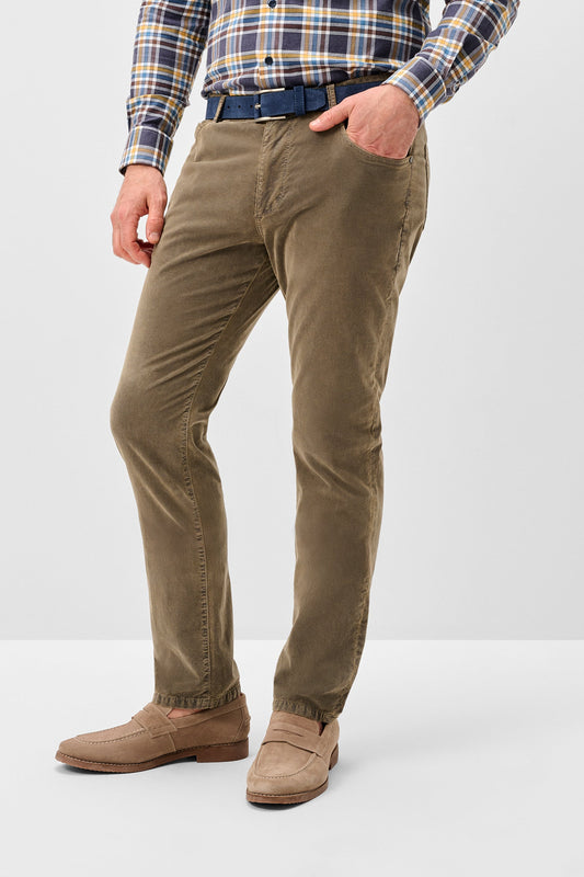 A person wearing slim-fit olive brown corduroy trousers, styled with a blue belt, a blue and yellow plaid shirt, and tan loafers, shown from the waist down on a light gray studio background.