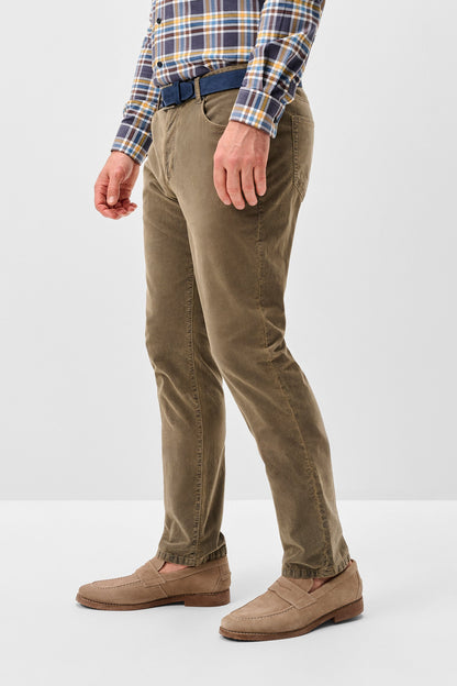 A person wearing slim-fit olive brown trousers, styled with a blue belt, a blue and yellow plaid shirt, and tan suede loafers, shown from the waist down against a light gray studio background.