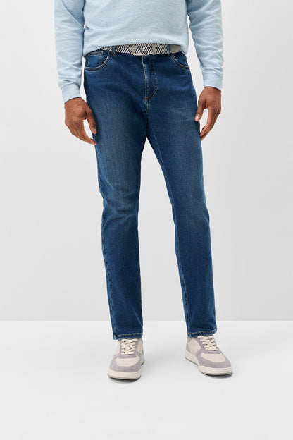 A person wearing medium-wash blue jeans, a light blue long-sleeve top, and gray sneakers, shown from the waist down against a plain light gray studio background.