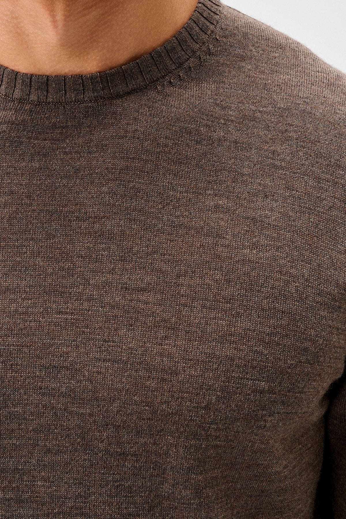 Close-up of a person wearing a dark brown ribbed knit crewneck sweater, showing the texture of the fabric and the collar.