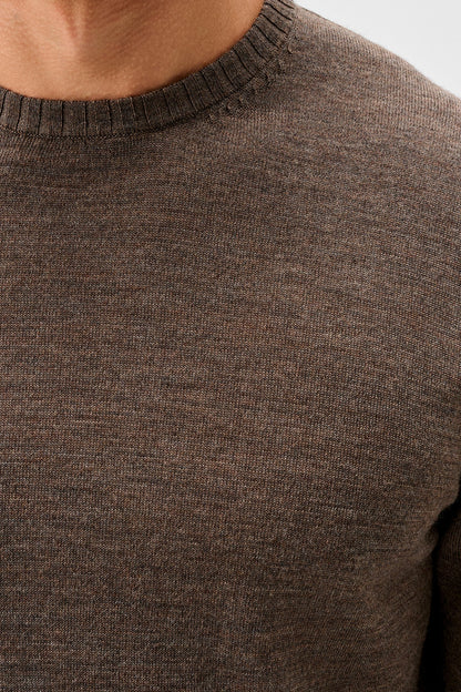 Close-up of a person wearing a dark brown ribbed knit crewneck sweater, showing the texture of the fabric and the collar.