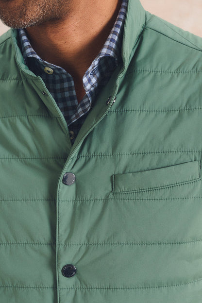 Close-up of a man wearing a sage green quilted puffer vest over a blue and white checkered button-down shirt.