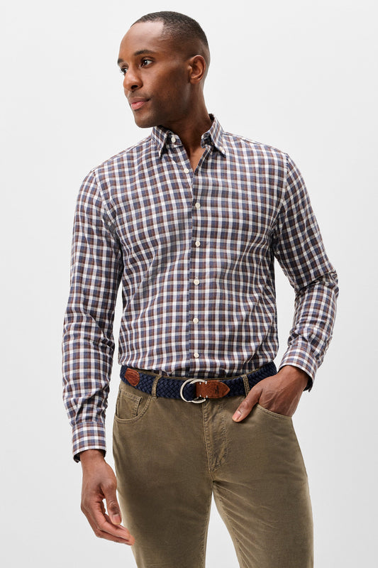 A man wearing a long-sleeve button-down shirt with a brown, white, and blue checkered pattern, paired with olive green trousers and a patterned belt, photographed against a light gray studio background.