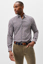 A man wearing a long-sleeve button-down shirt with a brown, white, and blue checkered pattern, paired with olive green trousers and a patterned belt, photographed against a light gray studio background.