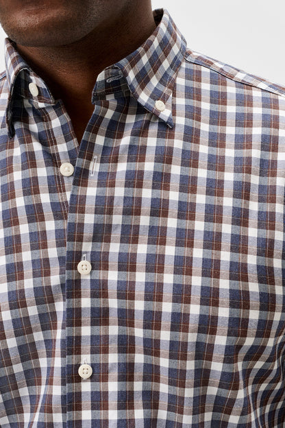 Close-up of a man wearing a plaid button-down shirt with a blue, brown, and white checkered pattern.