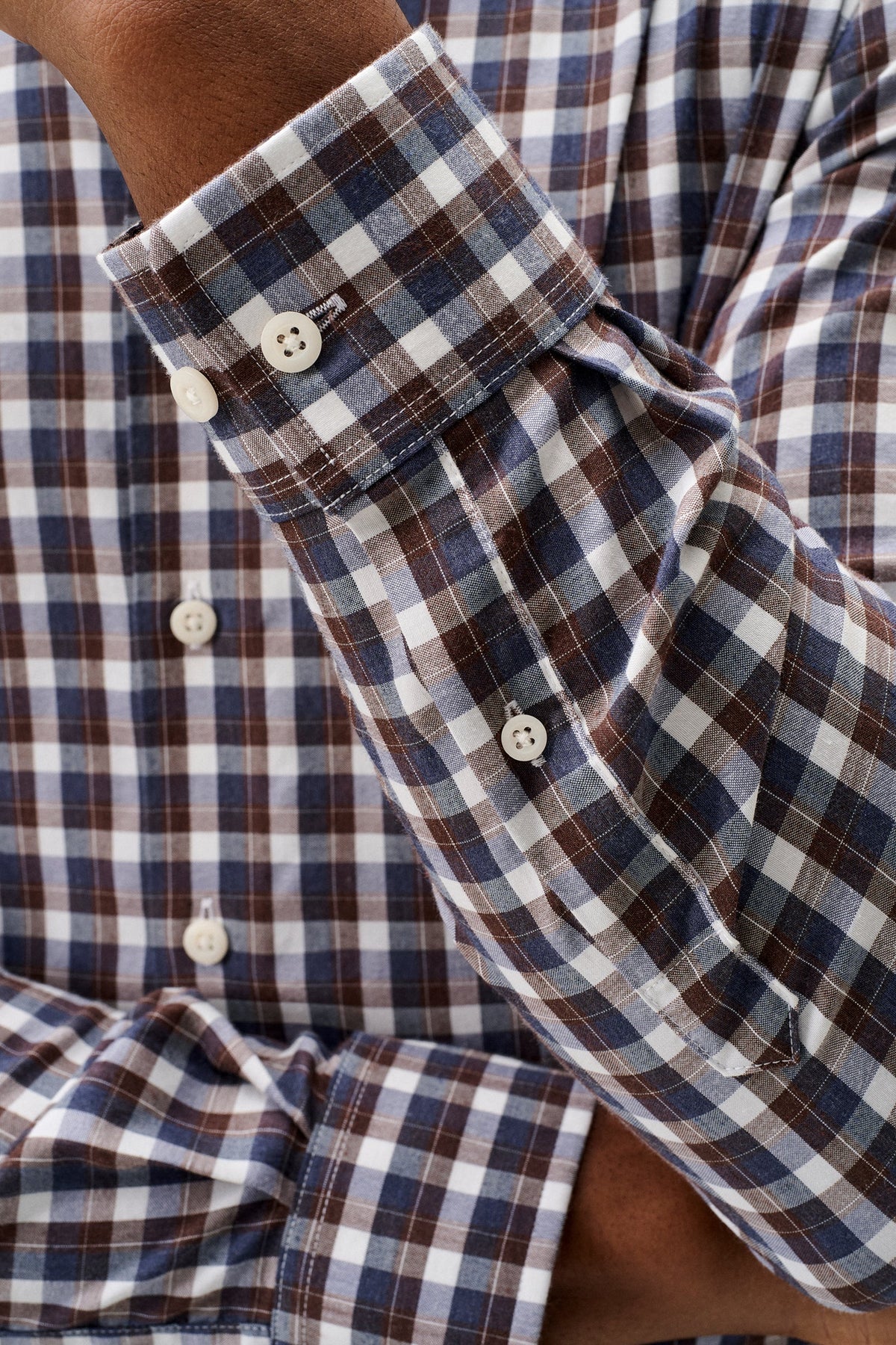 Close-up of a man wearing a long-sleeve plaid button-down shirt, showing the cuff, buttons, and fabric pattern.