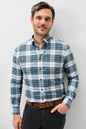 A man wearing a long-sleeve plaid button-down shirt in blue, green, and white, paired with a brown belt and dark gray trousers, standing against a light gray background.