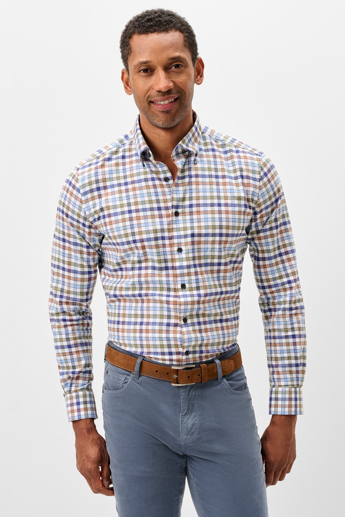 A man wearing a long-sleeve button-down shirt with a multicolor plaid pattern in blue, orange, and white, paired with blue jeans and a brown belt, against a light gray studio background.