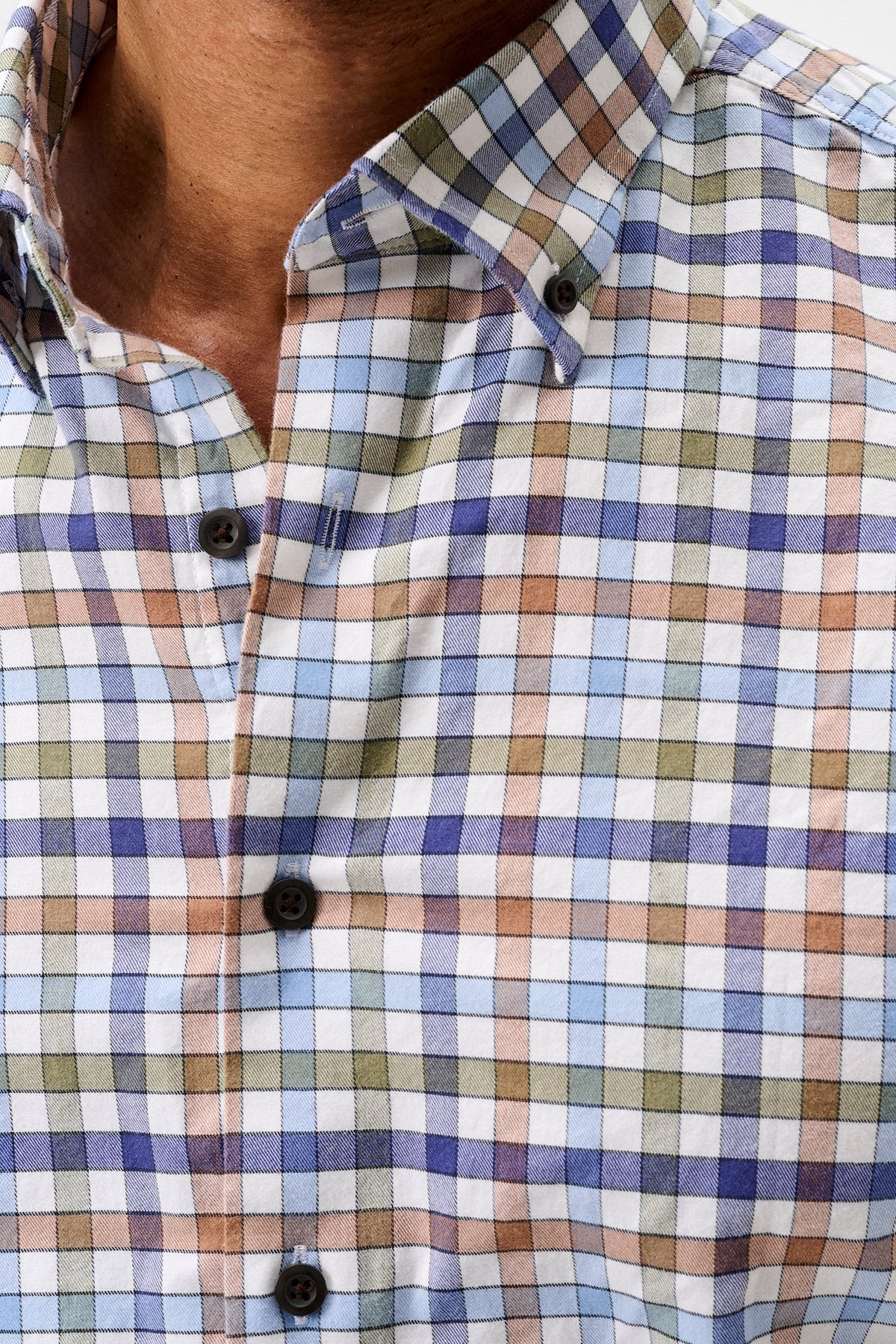 Close-up of a man wearing a long-sleeve button-down shirt with a multicolor plaid pattern in blue, green, orange, and white.