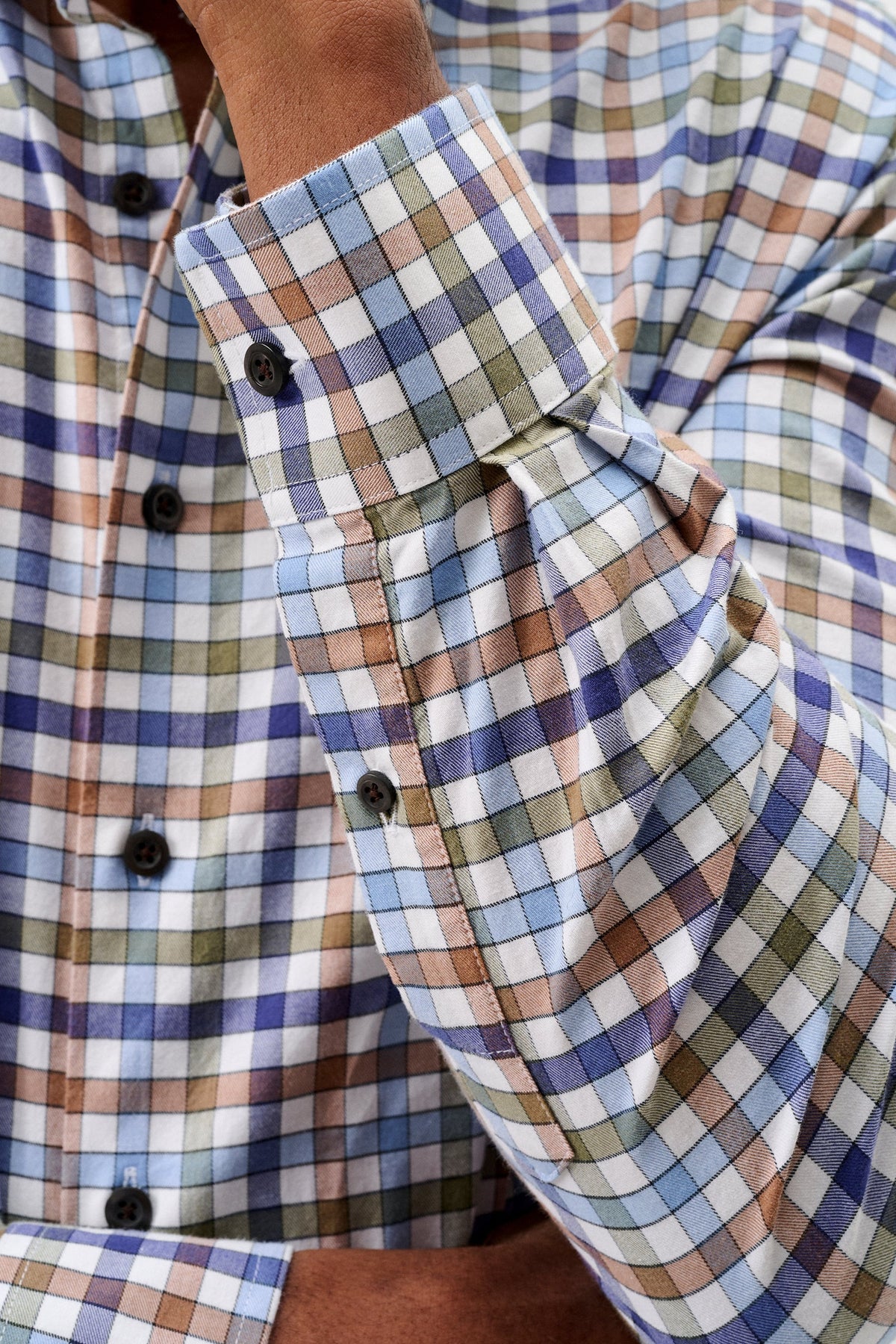 Close-up of a man wearing a long-sleeve plaid button-down shirt with a blue, brown, and white checkered pattern.