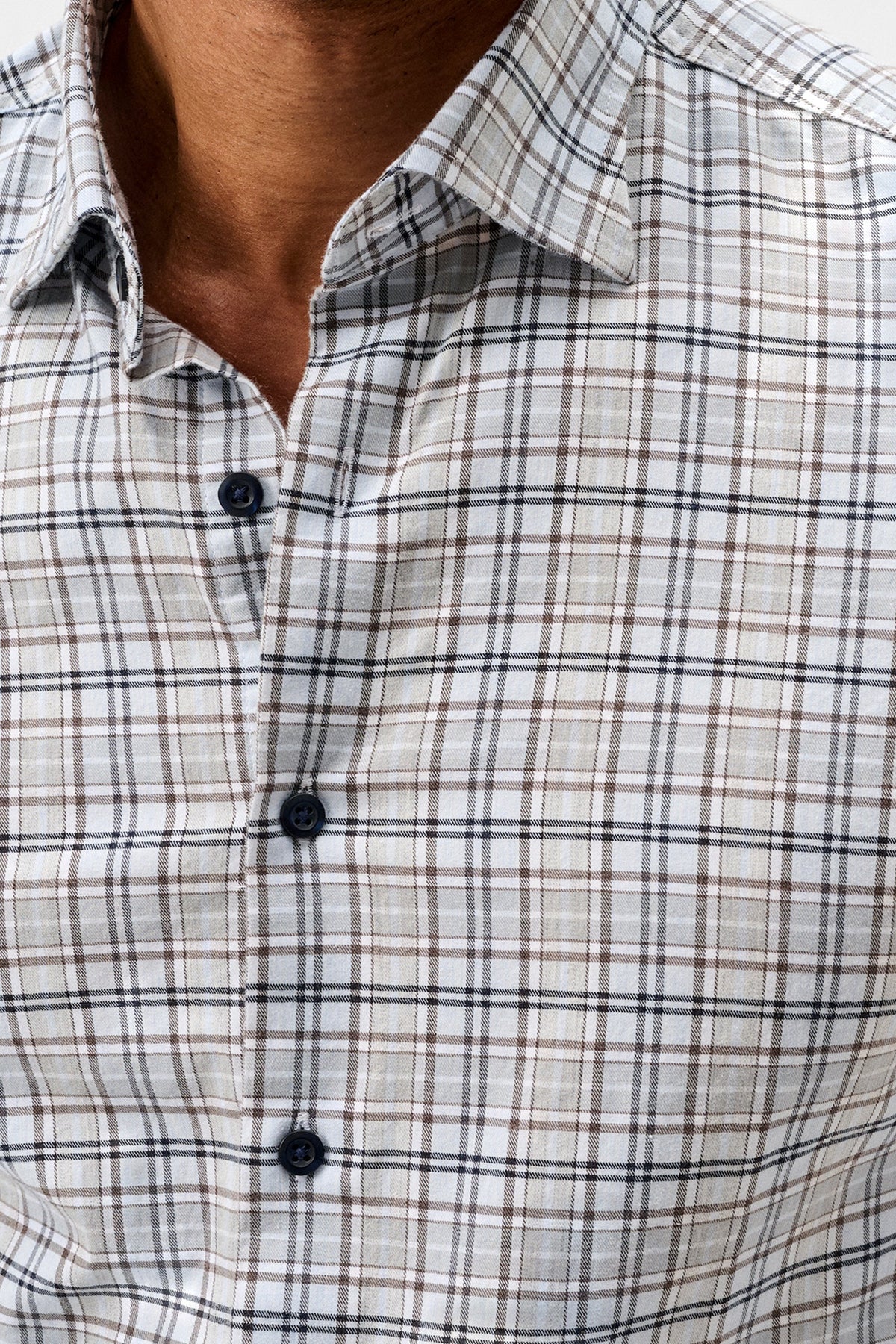 Close-up of a man wearing a long-sleeve plaid button-down shirt in beige, white, and brown with thin black lines.