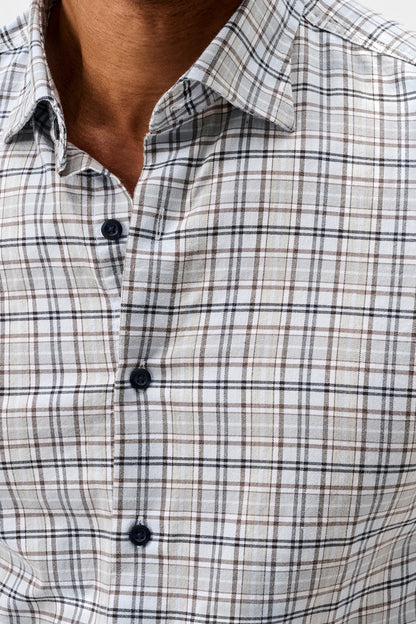 Close-up of a man wearing a long-sleeve plaid button-down shirt in beige, white, and brown with thin black lines.