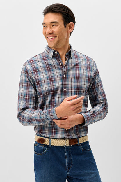 A man wearing a long-sleeve button-down plaid shirt in blue, red, and white, paired with blue jeans and a patterned belt, standing against a light gray studio background.