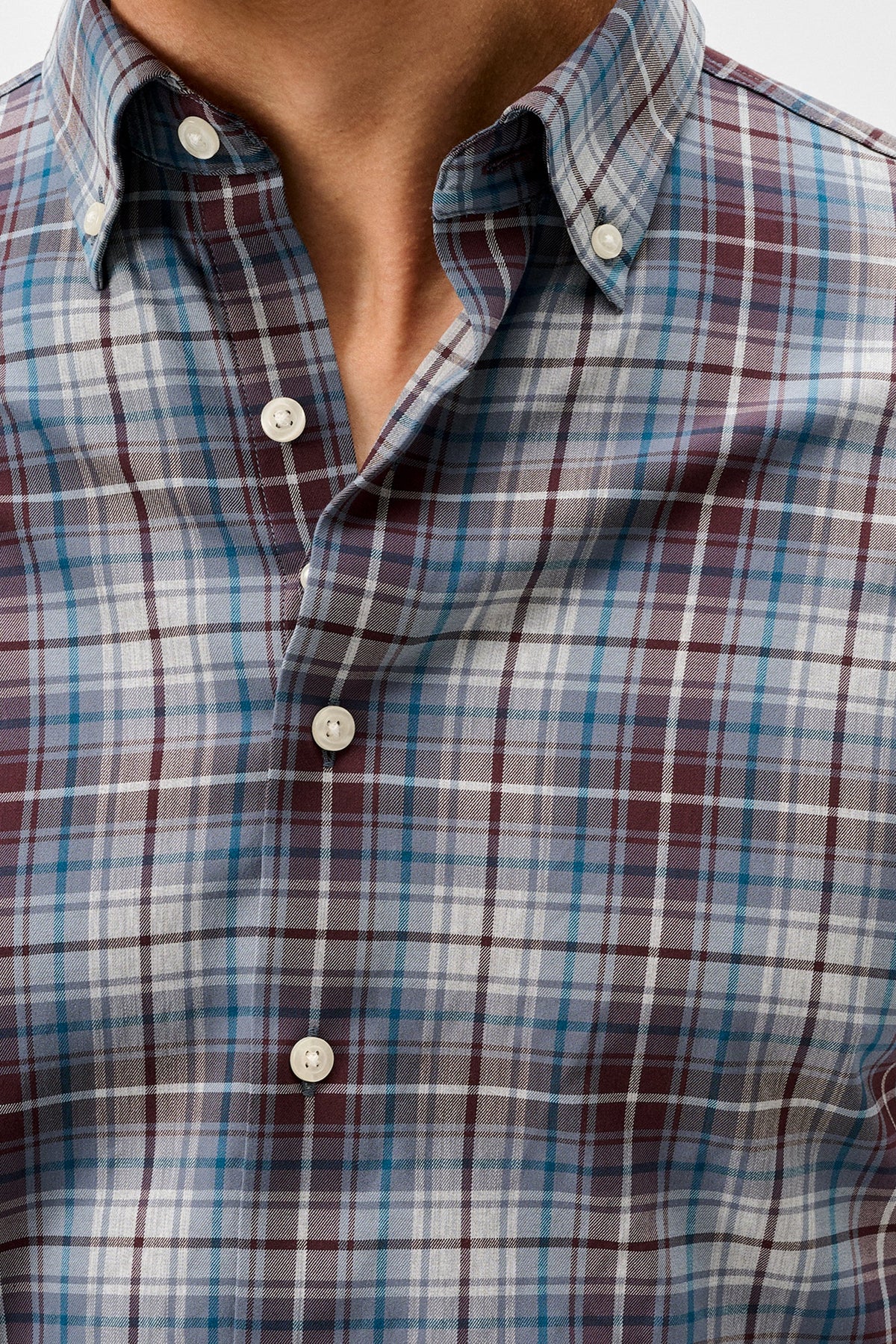 Close-up of a men's button-down plaid shirt worn by a model, featuring a pattern of blue, burgundy, and white intersecting plaid lines.