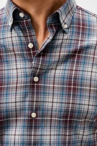 Close-up of a men's button-down plaid shirt worn by a model, featuring a pattern of blue, burgundy, and white intersecting plaid lines.