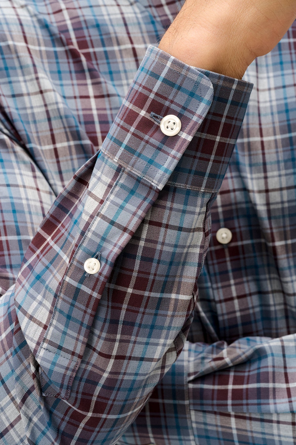 Close-up of a plaid button-down shirt sleeve with a cuff, featuring white buttons and a pattern of blue, burgundy, and gray intersecting lines.