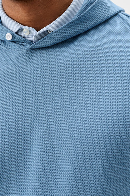 Close-up of a light blue textured polo shirt with a hood, worn over a light blue and white striped collared shirt.