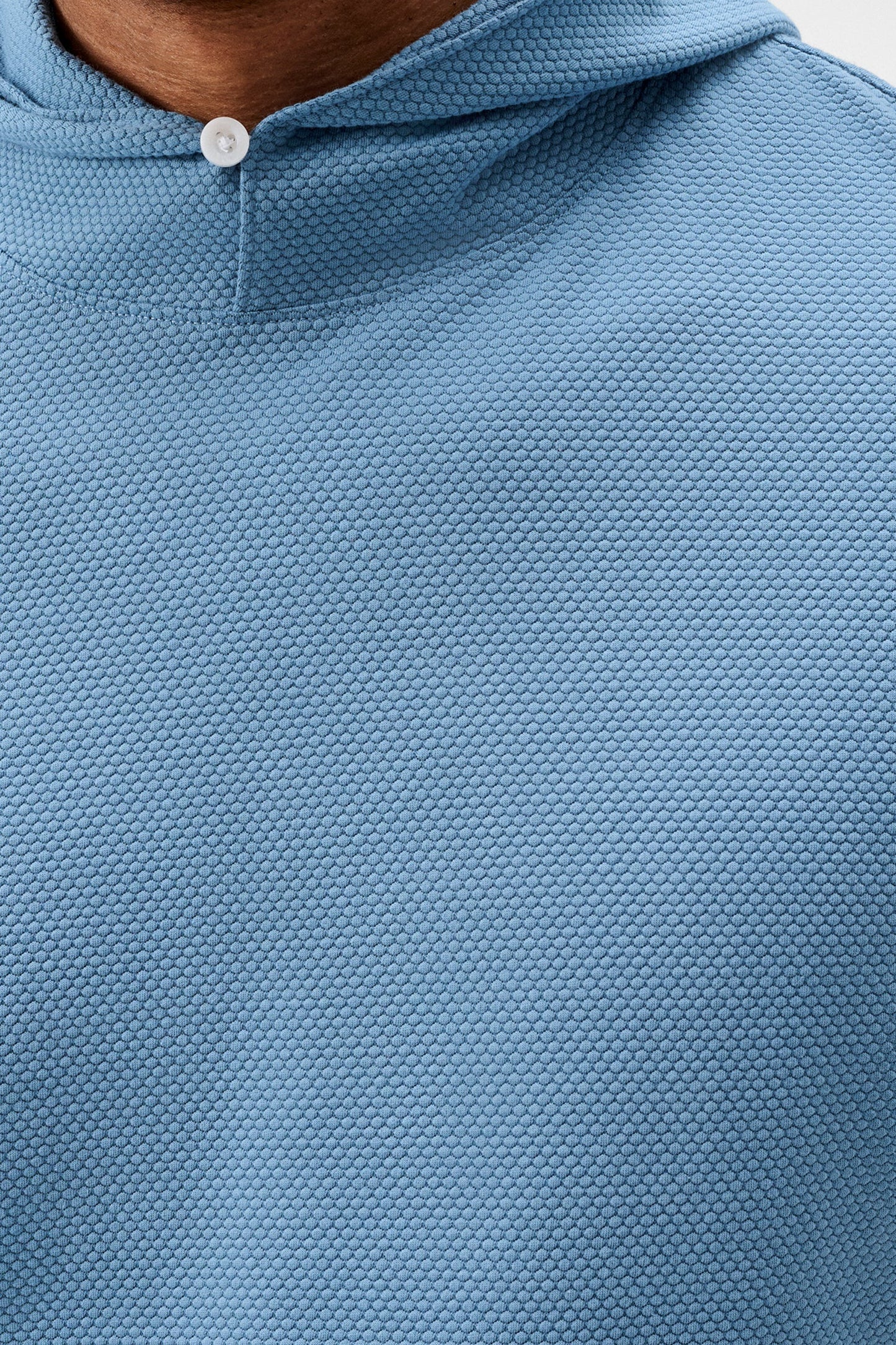 Close-up of a person wearing a textured light blue hooded pullover top, showing the collar and chest area.
