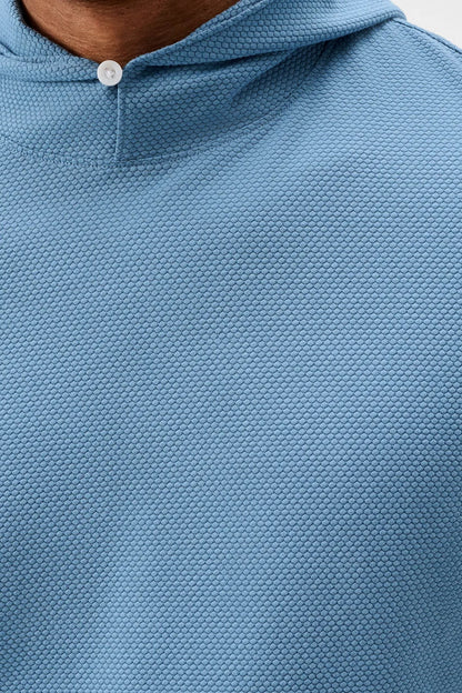 Close-up of a textured light blue hooded pullover top with a small white button at the collar, worn by a model.