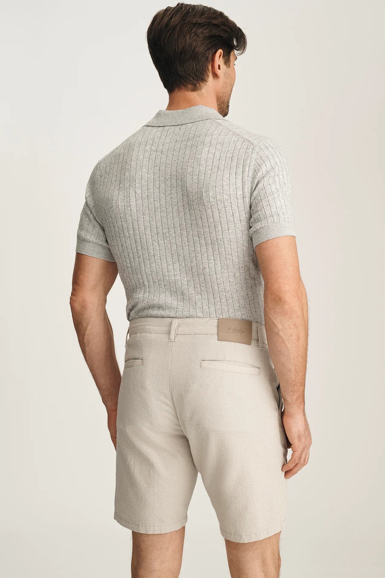 Man wearing a light gray checkered polo shirt and beige shorts on a plain background