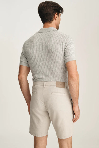 Man wearing a light gray checkered polo shirt and beige shorts on a plain background
