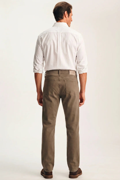 A man viewed from the back wearing a white long-sleeve button-down shirt and brown trousers, standing against a plain light background.