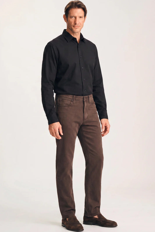A man modeling a black long-sleeve button-down shirt and brown trousers against a plain light gray studio background.