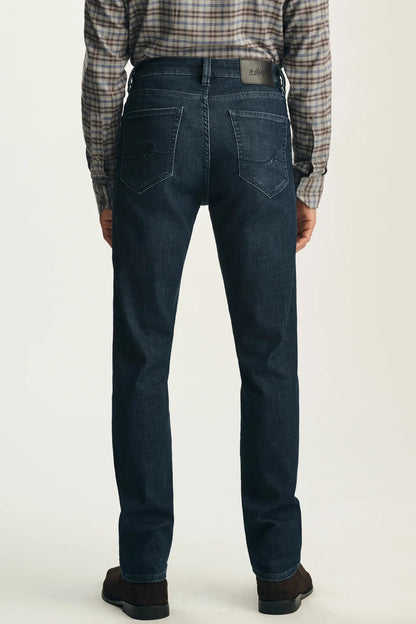Rear view of a person wearing dark blue denim jeans and a brown and beige plaid shirt, standing against a plain light background.