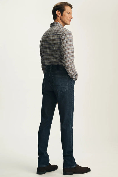 A man shown from the back wearing a gray and brown plaid button-down shirt and dark blue jeans, standing against a plain off-white studio background.