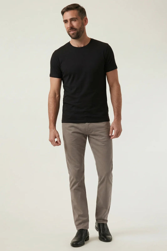 A man modeling a black short-sleeve crewneck t-shirt and light brown trousers against a plain light gray studio background.