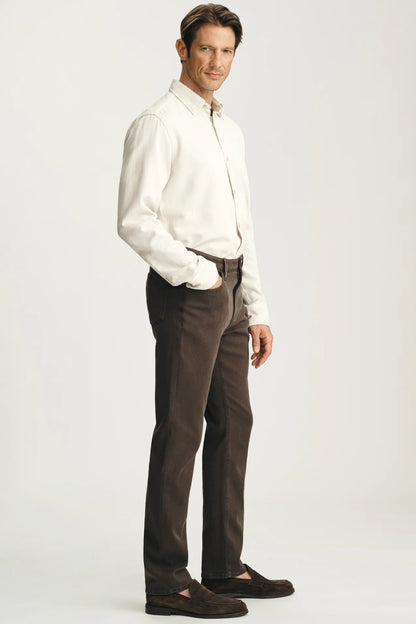 A man modeling a white long-sleeve button-down shirt and dark brown trousers, paired with dark brown loafers, against a light gray studio background.