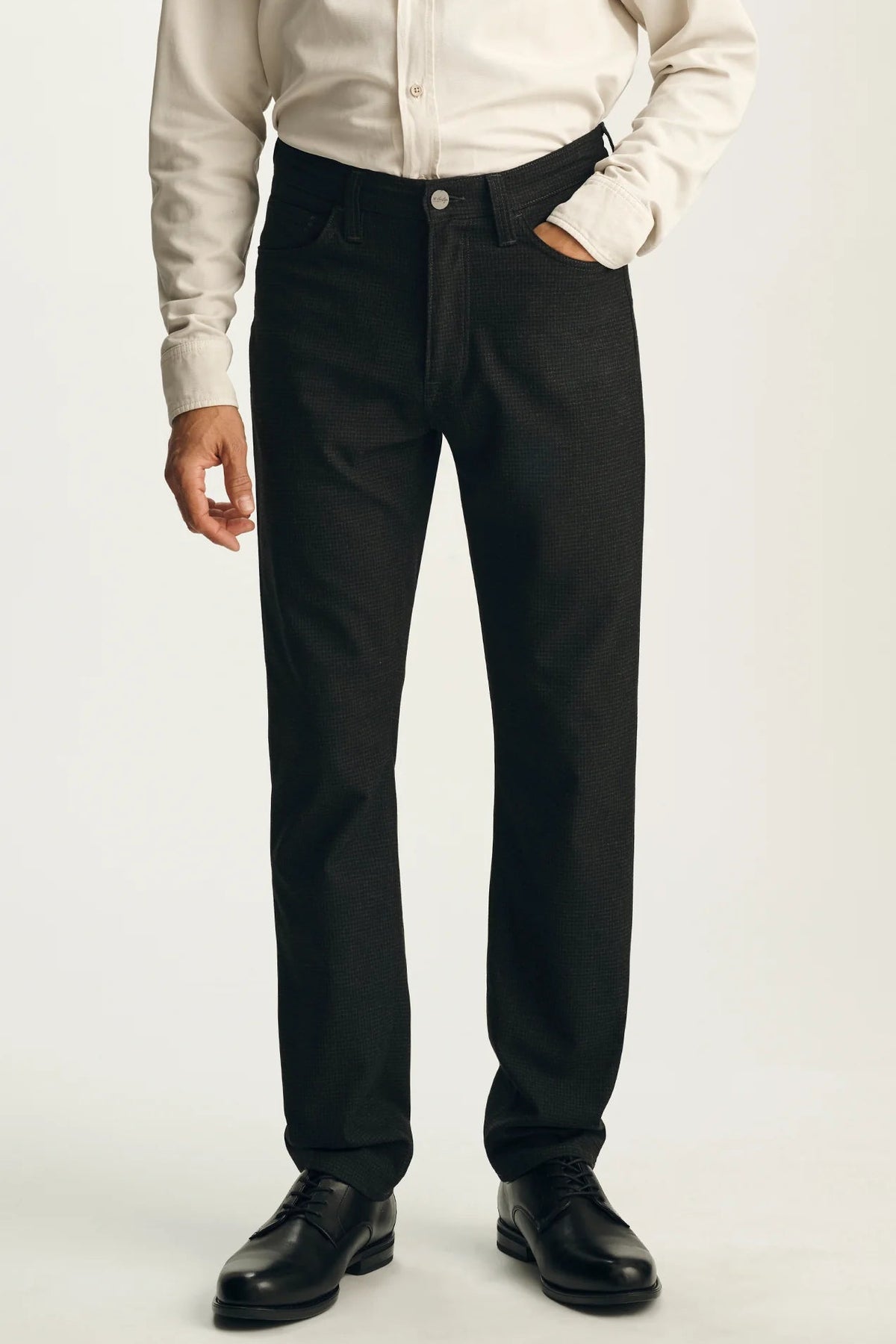 A person wearing black straight-leg dress pants with a cream button-up shirt and black leather shoes, shown from the chest down against a light gray studio background.