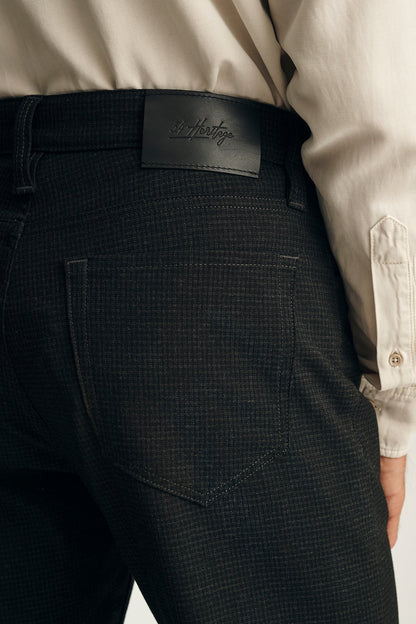 Close-up of the back waist of a person wearing dark charcoal textured trousers with a black leather patch showing the embossed brand 'Hustey', paired with a light beige button-down shirt.