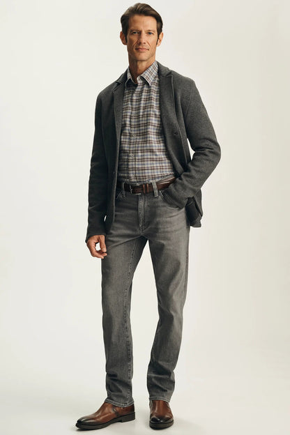 A man modeling a gray blazer, gray plaid shirt, gray jeans, and brown leather dress shoes against a light gray studio background.