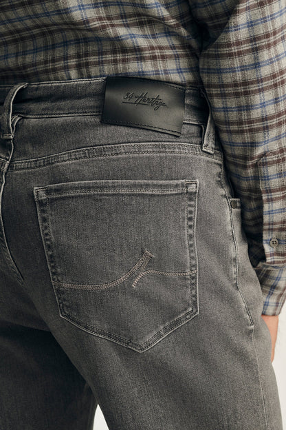 Close-up of the back waistband of dark gray washed denim jeans, showing a black leather patch with the 'Softer' brand logo, worn with a plaid shirt.