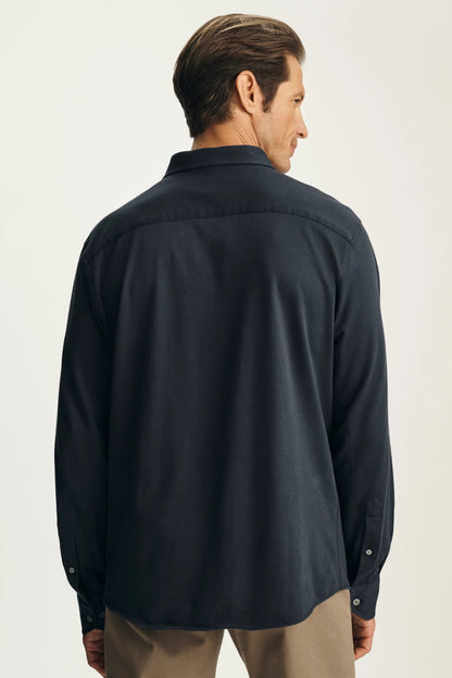 A man shown from the back wearing a dark navy long-sleeve button-up shirt and khaki pants, photographed against a clean off-white studio background.