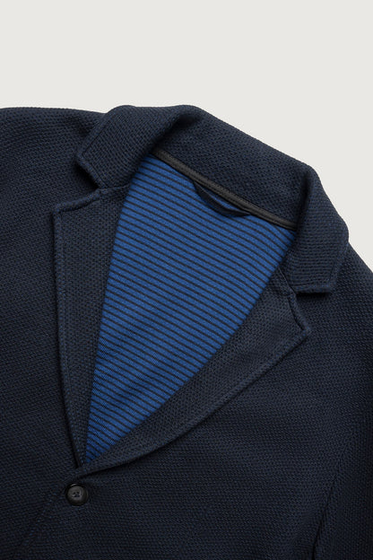 Close-up of a dark navy textured blazer jacket with a buttoned collar, showing a blue and navy striped knit shirt underneath.