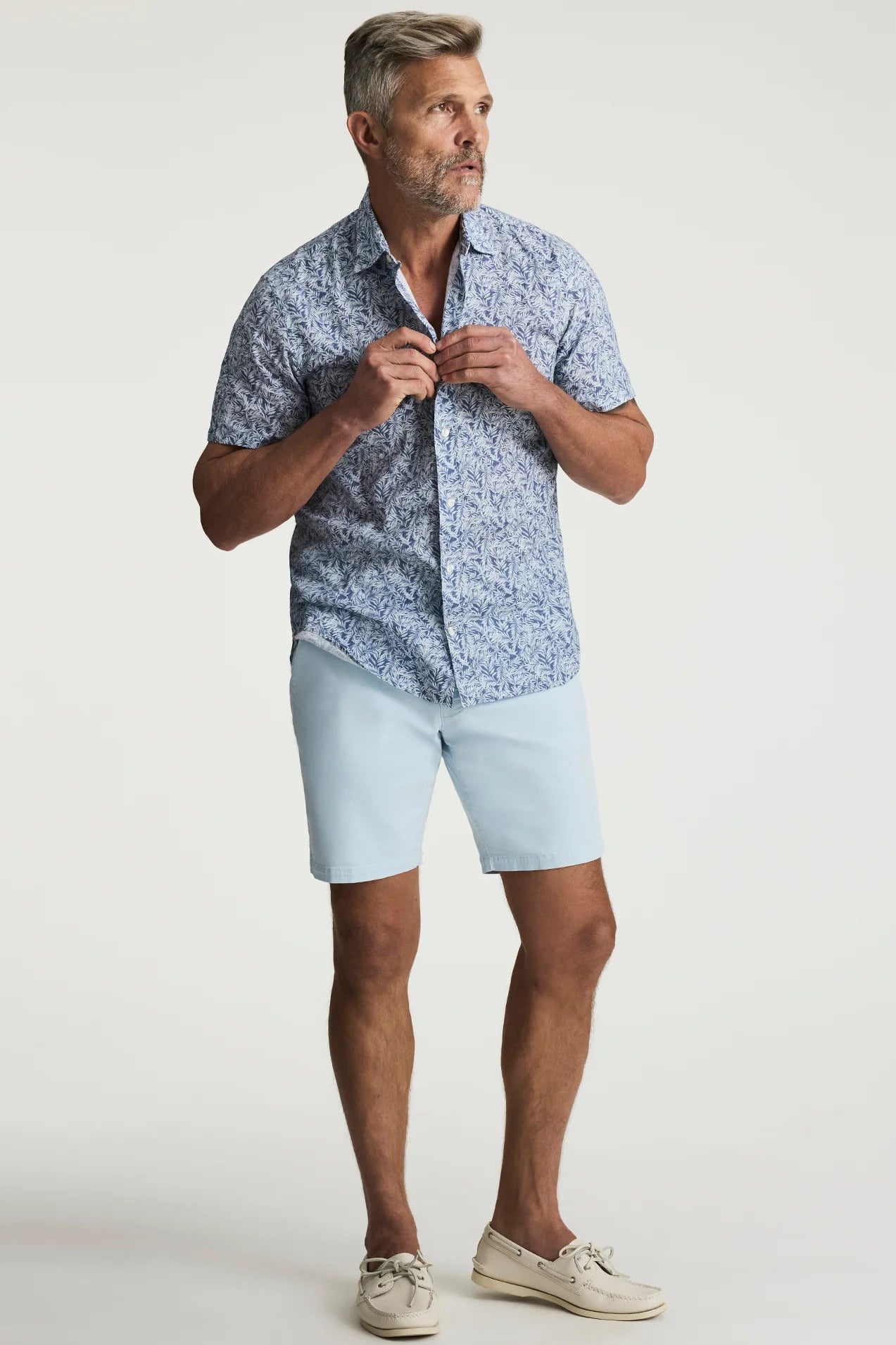 Man wearing a blue patterned shirt and light blue shorts on a white background