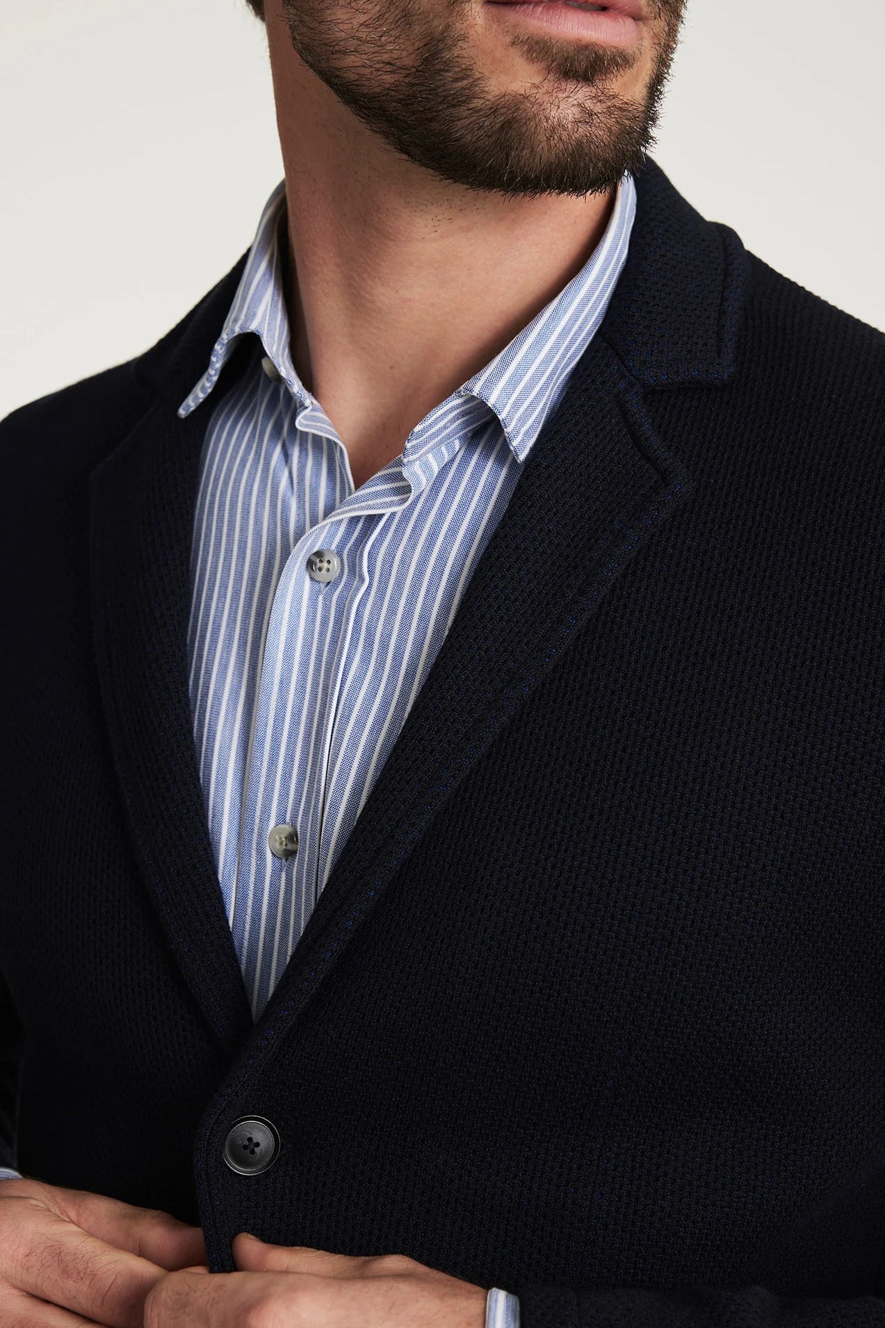 Man wearing a dark coat over a striped shirt with a neutral background
