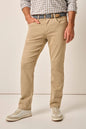 A man wearing beige slim-fit chino pants, a patterned belt, a checkered shirt, and light-colored sneakers, standing against a plain beige studio background.