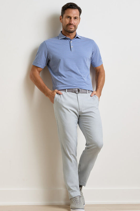 Man wearing a blue striped polo shirt and light gray pants against a plain background