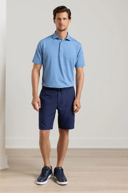 Man wearing a blue polo shirt and navy shorts standing against a plain background