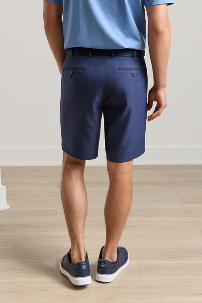 Person wearing navy shorts and blue shoes on a wooden floor.