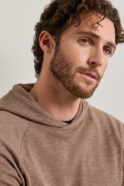 A close-up shot of a man wearing a heathered brown pullover hoodie against a light gray background.