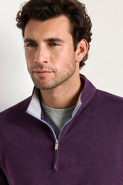 A man wearing a purple quarter-zip pullover sweater with a light gray inner placket and a gray t-shirt underneath, photographed against a light gray studio background.