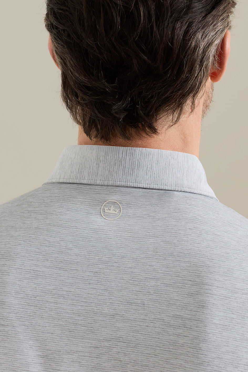 Gray polo shirt with a brand logo on the collar against a beige background