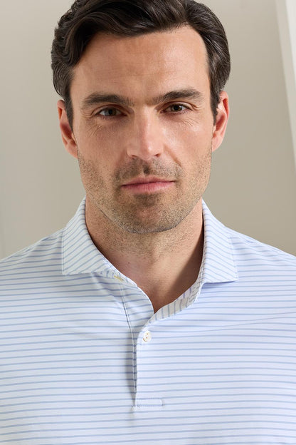 A close-up shot of a man wearing a light blue and white striped polo shirt, photographed against a soft beige background.