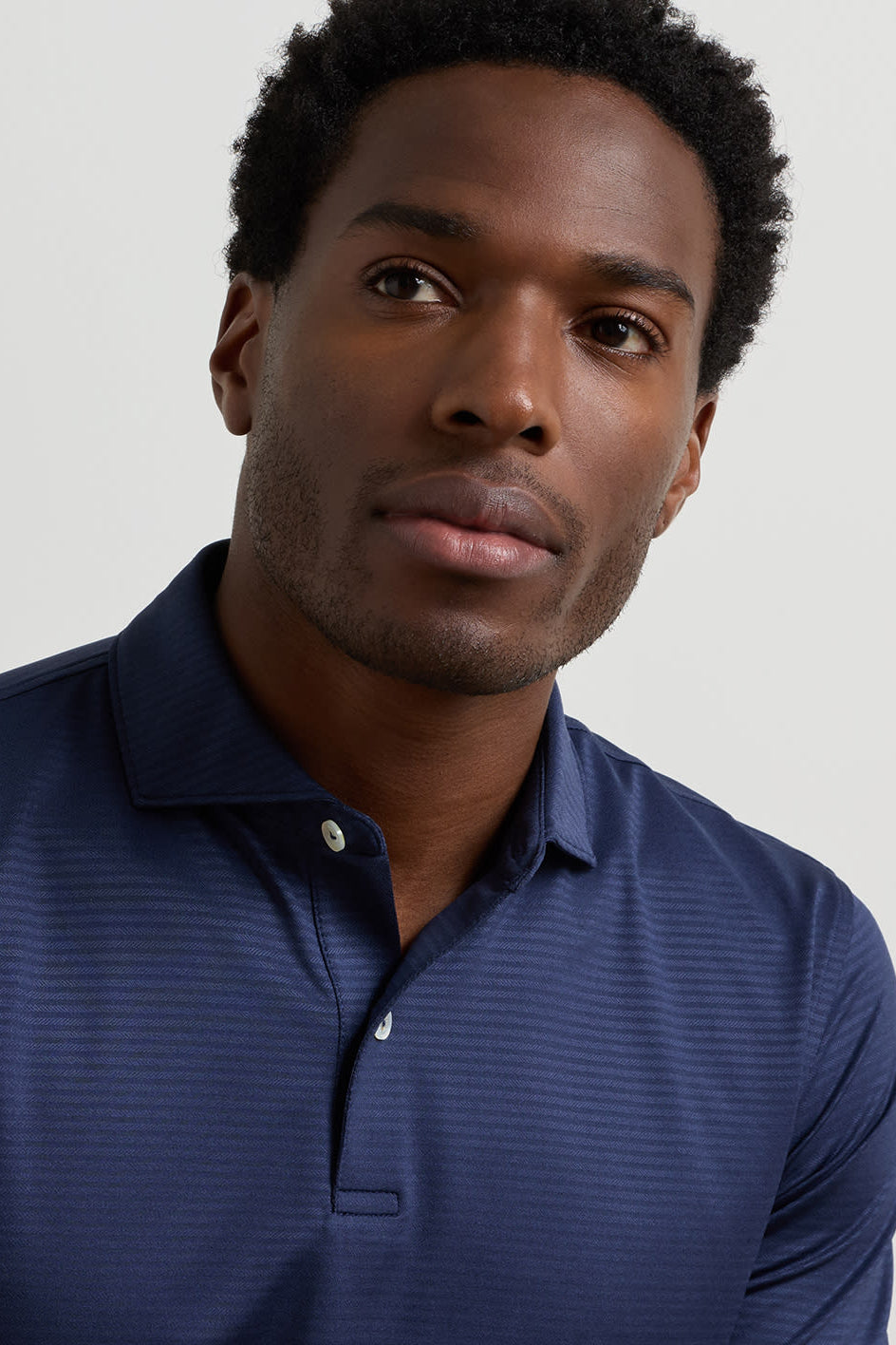 A close-up shot of a man wearing a navy blue long-sleeve polo shirt with a subtle textured pattern, set against a plain light gray background.